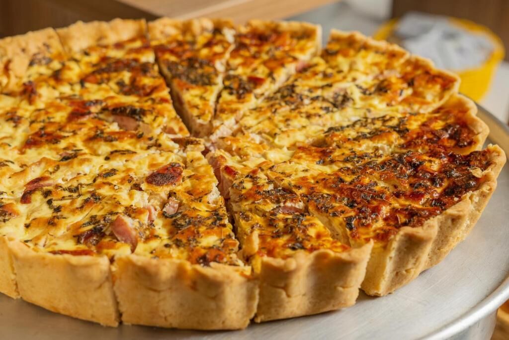 A round pizza with a golden-brown crust, cut into slices, and topped with melted cheese and herbs.