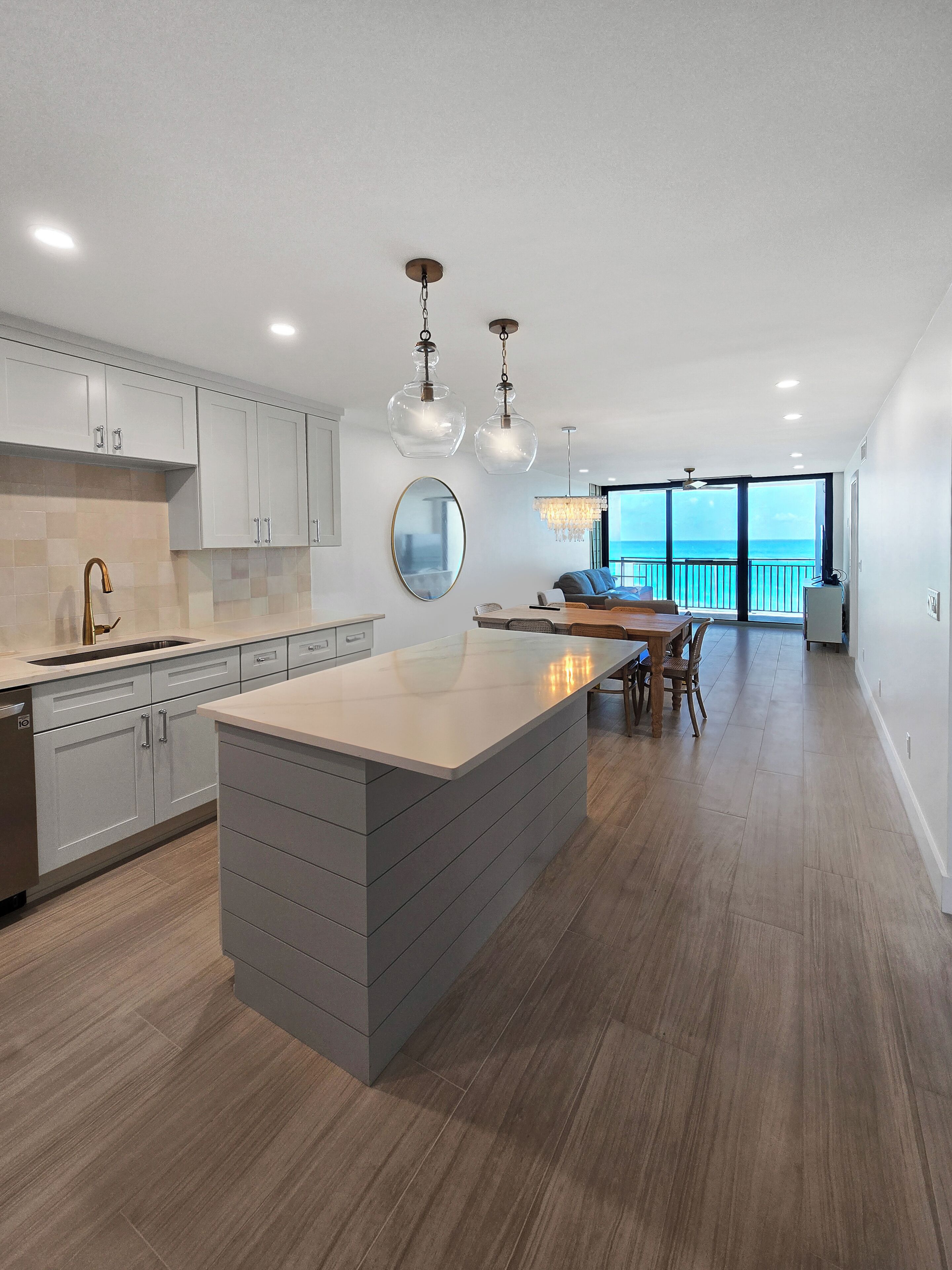 A modern kitchen with a large island, white cabinets, and a view to the outside.