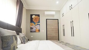 A hotel room with a bed, a wardrobe, a painting on the wall, and an air conditioning unit.