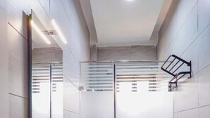 A modern bathroom with a glass shower enclosure, a towel rack, and a visible ceiling light.