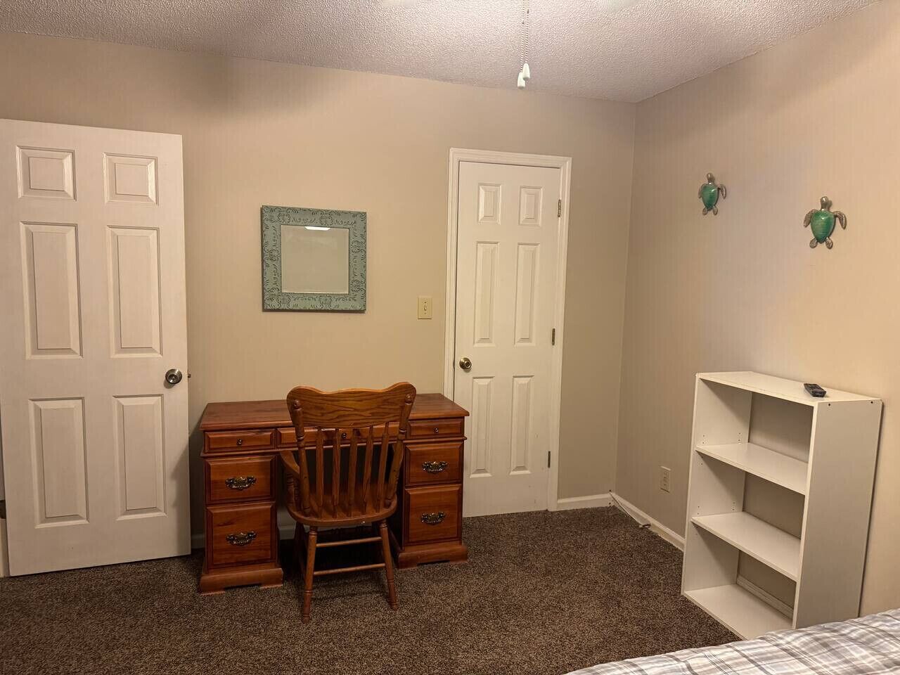 A bedroom with two white doors, a wooden dresser, a chair, and a white shelving unit.