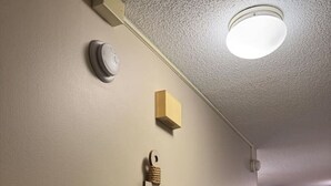 Een kamer met een beige muur, een plafondlamp, een rookmelder en een houten ankerdecoratie.