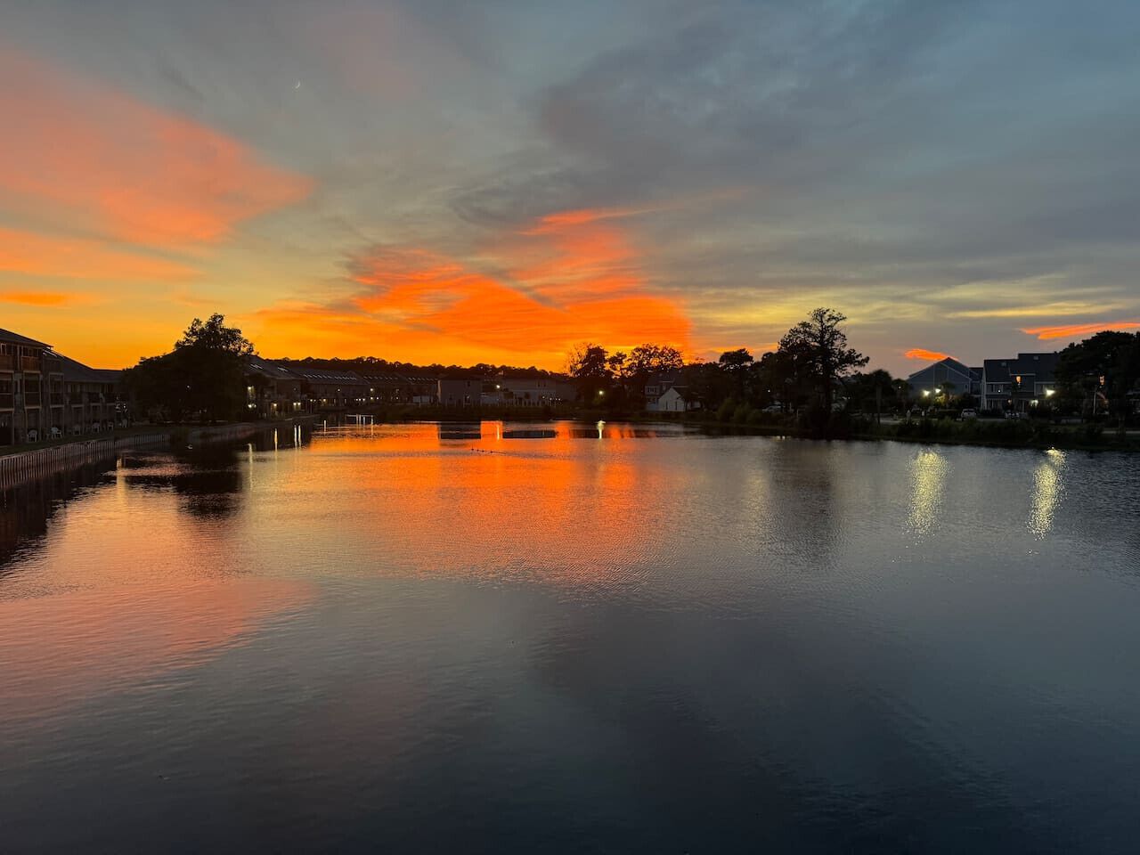 A calm river reflecting a sunset with buildings on the opposite bank.