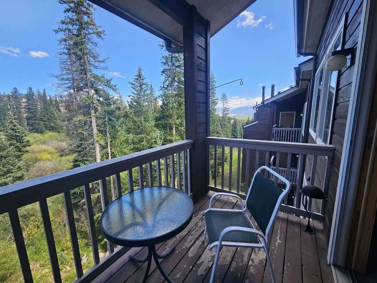 A wooden deck with a round table and two chairs, overlooking a forested area.
