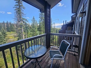 A wooden deck with a round table and two chairs, overlooking a forested area.