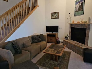 A living room with a sofa, a coffee table, a TV, a fireplace, and a staircase.