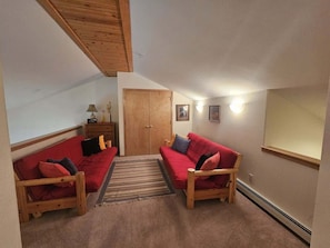 A cozy living room with two red sofas, a wooden cabinet, and a door.