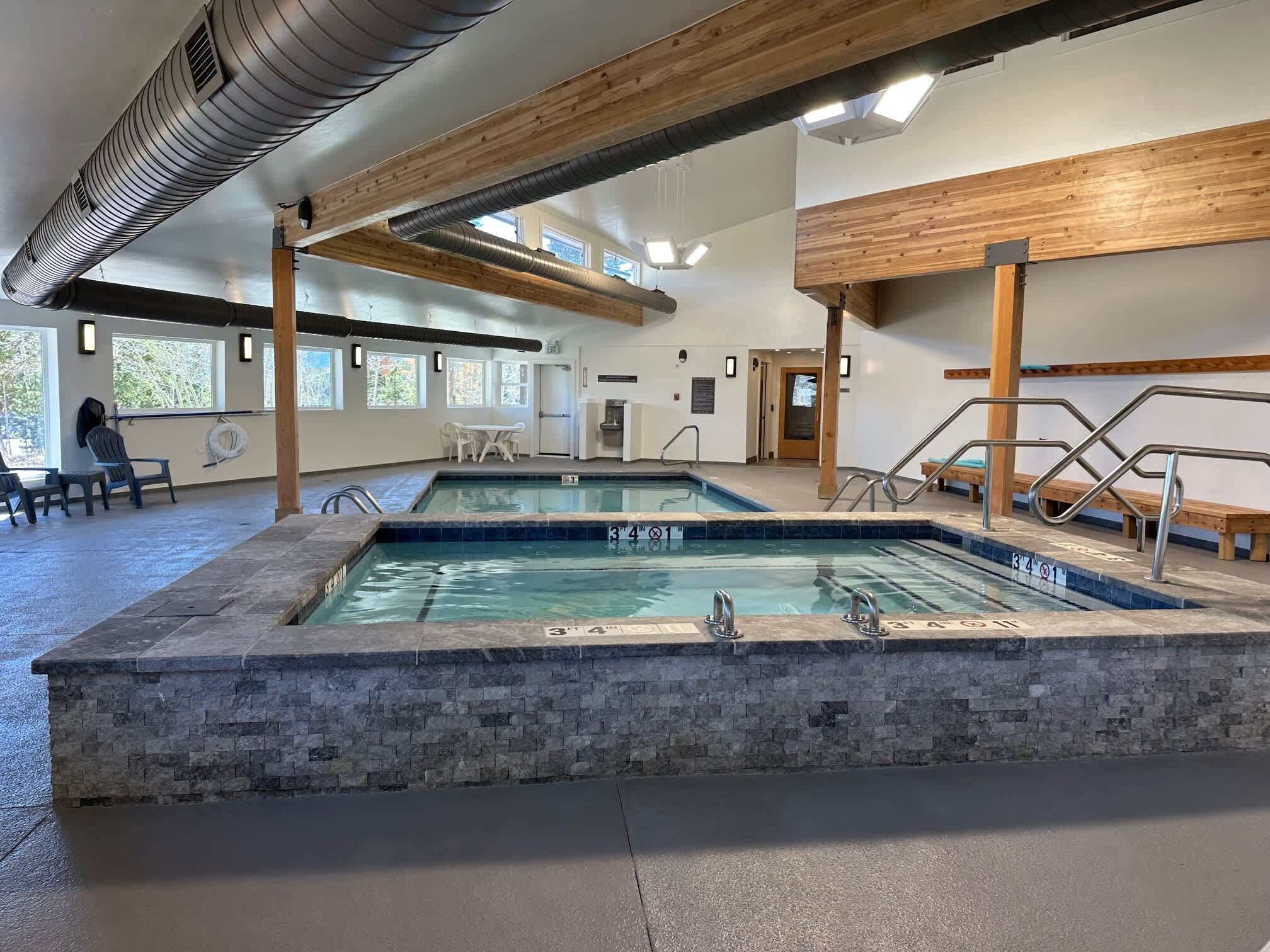 An indoor swimming pool with clear water, surrounded by stone walls and wooden beams.