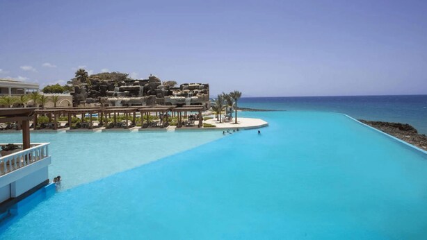 Un resort con una piscina grande, una estructura rocosa con cascada y vistas al océano.