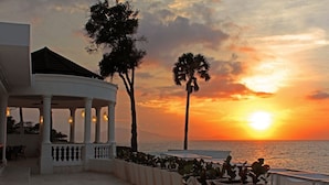 A gazebo with columns, a palm tree, and a sunset over the ocean. - Sosua Ocean Village (Sosúa)