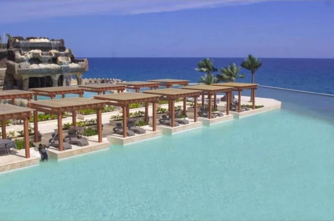 A resort pool area with a clear view of the ocean, lounge chairs, and a unique stone structure.