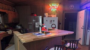 A kitchen with a wooden island, bar stools, a neon sign, a refrigerator, and a water dispenser.