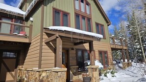 A two-story wooden house with a stone foundation, a balcony, and a snow-covered roof.