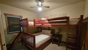 A bedroom with bunk beds, a ceiling fan, a window, and a small bedside table.