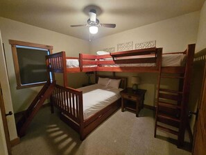 A bedroom with bunk beds, a ceiling fan, a window, and a small bedside table.