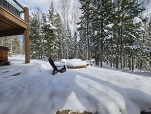 A snow-covered outdoor area with a wooden deck, a black chair, and a round wooden table.