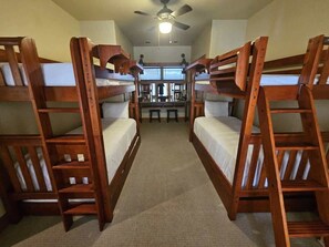 A room with two wooden bunk beds, a ceiling fan, and a window providing natural light.