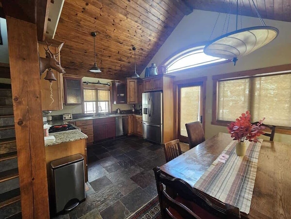 A rustic kitchen with wooden cabinets, a refrigerator, and a dining table with chairs.