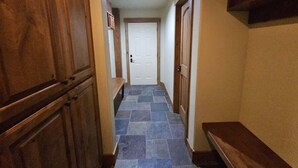 A narrow hallway with a tiled floor, wooden cabinets, and a door at the end.