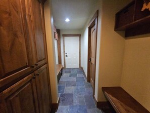 A narrow hallway with a tiled floor, wooden cabinets, and a door at the end.