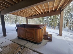 A hot tub under a wooden pergola in a snowy outdoor setting.