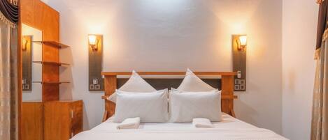A hotel room with a wooden headboard, two wall-mounted lights, a wooden wardrobe, and a bed with white bedding.