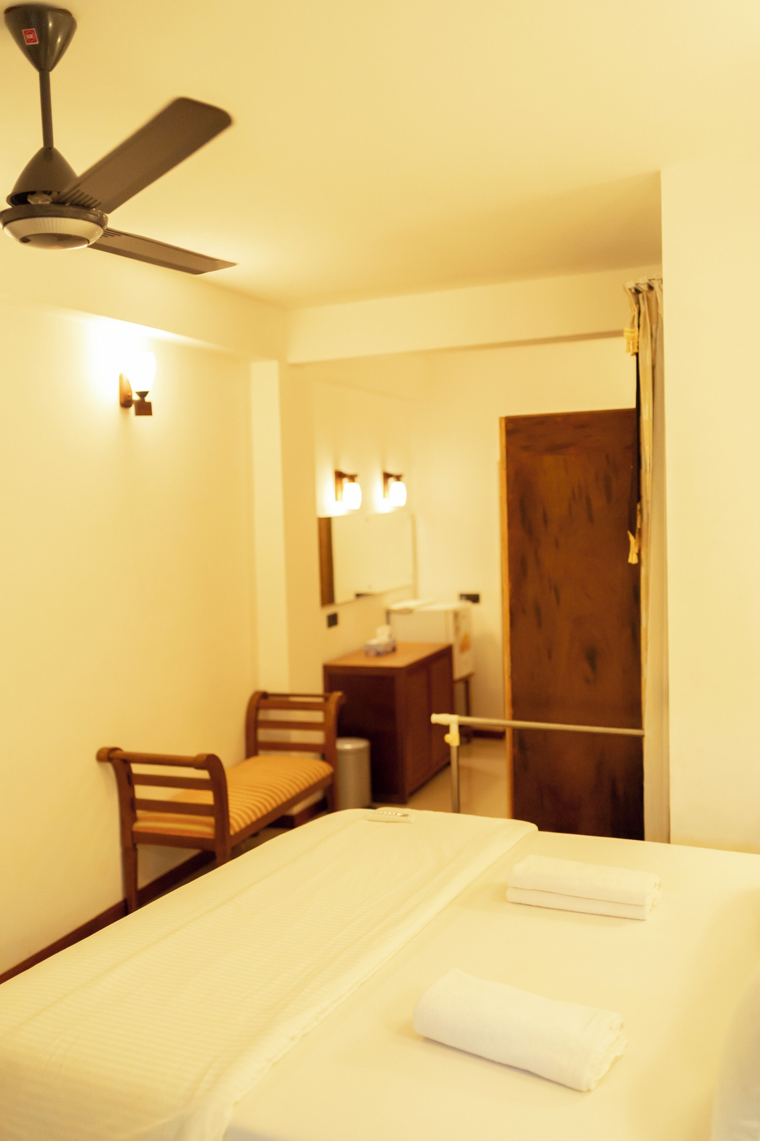 Una habitación de hotel con una cama, un escritorio, una silla, un ventilador de techo y una puerta.