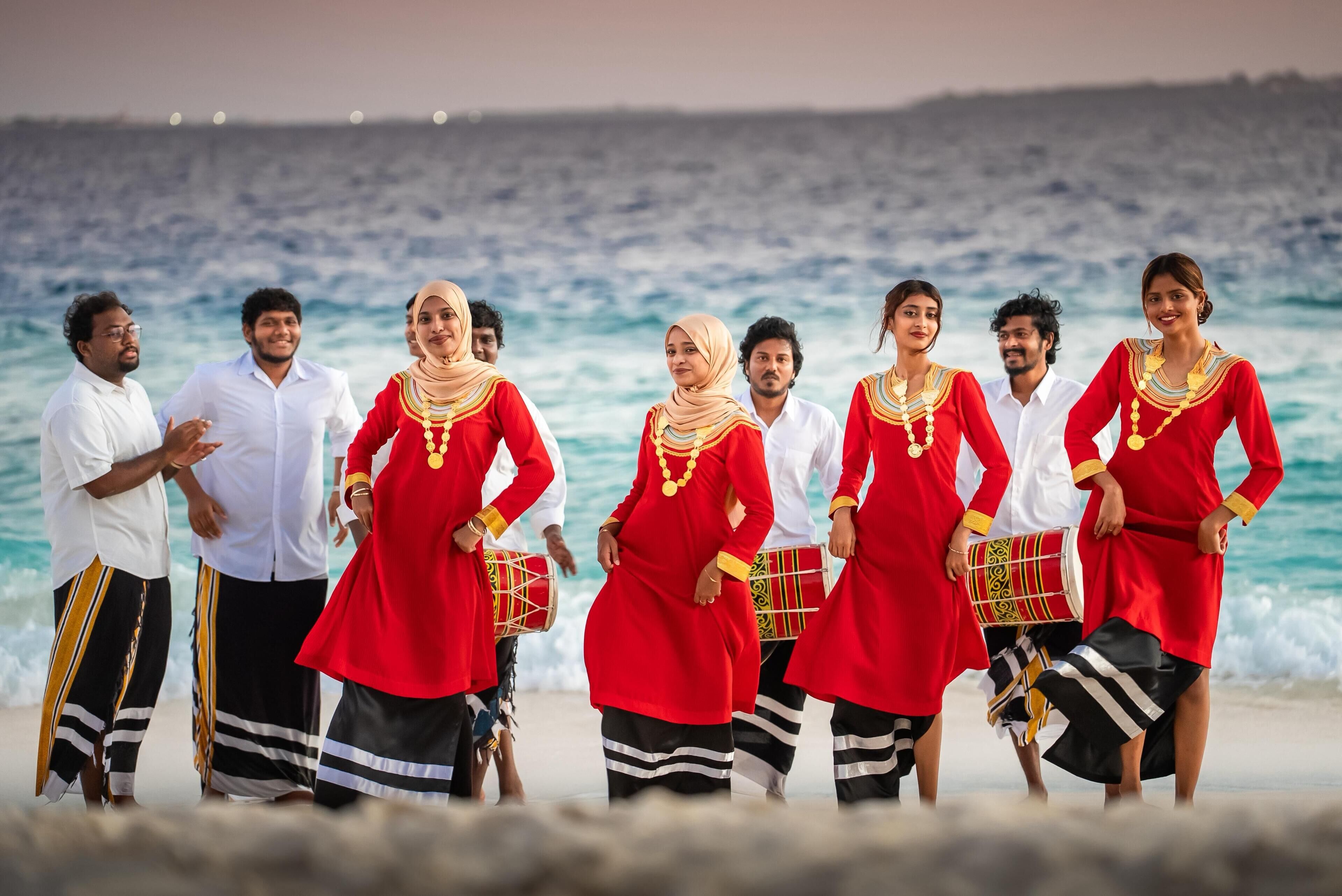 Un grupo de personas con vestimenta tradicional en una playa, con el océano al fondo.