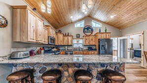 A kitchen with wooden cabinets, a stone island, and bar stools. - Heavenly Pines (Ruidoso)