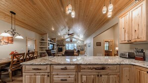 A spacious kitchen with wooden cabinets, a granite countertop, and pendant lighting. - Heavenly Pines (Ruidoso)
