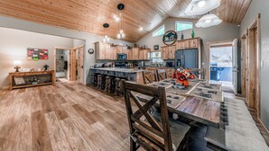 A spacious kitchen with wooden cabinets, a dining area with a large table, and a high ceiling with exposed beams. - Heavenly Pines (Ruidoso)