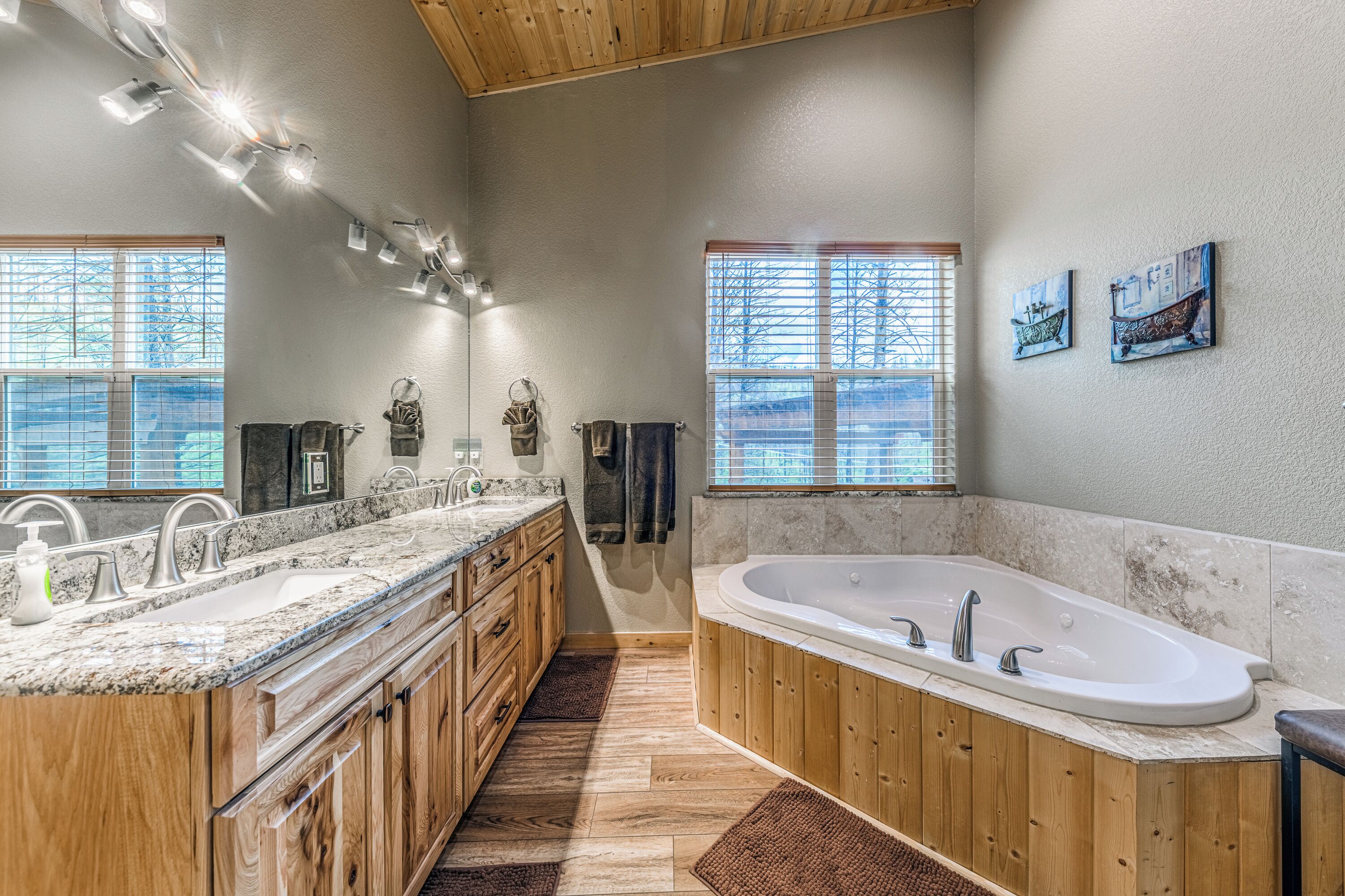 Un baño espacioso con una bañera grande, muebles de madera, encimeras de granito y ventanas amplias.