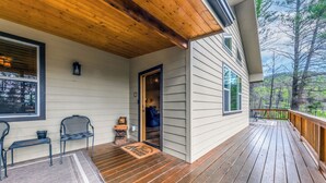 A wooden deck with a covered porch, a bench, and a welcome mat. - Heavenly Pines (Ruidoso)