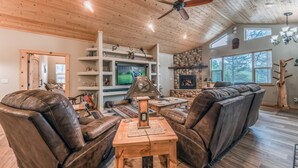 A spacious living room with a high ceiling, wooden beams, a fireplace, and a television. - Heavenly Pines (Ruidoso)