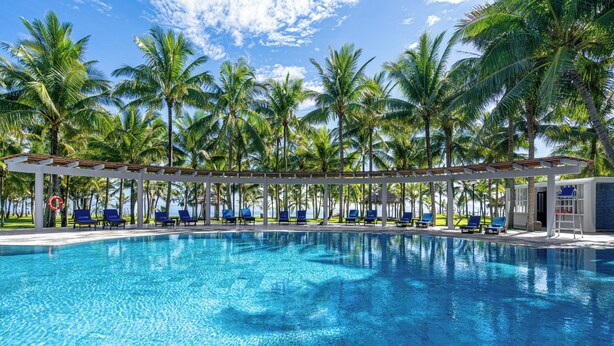Ein Pool mit blauem Wasser, umgeben von Palmen und blauen Liegestühlen.