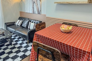 A living area with a sofa, a dining table with a checkered tablecloth, and a bowl of fruit. - Brooklyn Vibe Meets UPenn | Stylish 1BR | Sleeps 3 (Philadelphia)