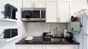 Une cuisine compacte avec des meubles blancs, un four à micro-ondes, une bouilloire et une machine à café.