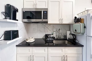 A modern kitchen with white cabinets, a black countertop, a microwave, a coffee maker, and a toaster. - Brooklyn Vibe Meets UPenn | Stylish 1BR | Sleeps 3 (Philadelphia)