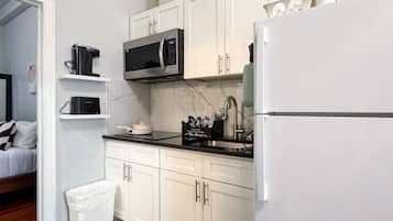 A modern kitchen with white cabinets, a black countertop, a microwave, a refrigerator, and a trash bin.