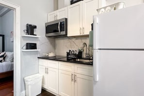 Une cuisine moderne avec des meubles blancs, un plan de travail noir, un four à micro-ondes, un réfrigérateur et une poubelle.