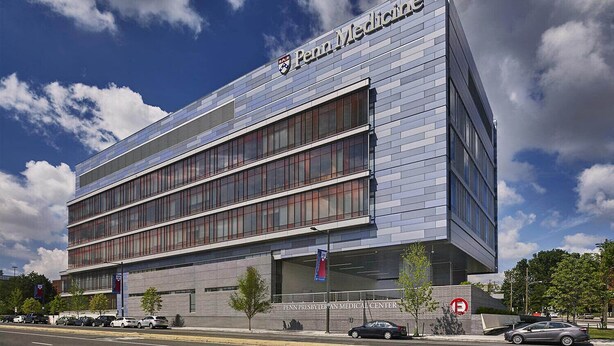 Un bâtiment moderne dont la façade porte l’inscription « Penn Medicine », avec une grande section de fenêtres en verre et une base en briques.