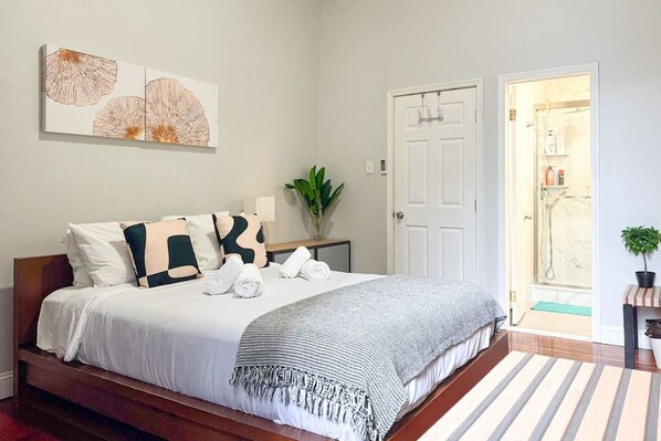 A bedroom with a bed, pillows, a bedside table with a lamp, and a door leading to a bathroom.