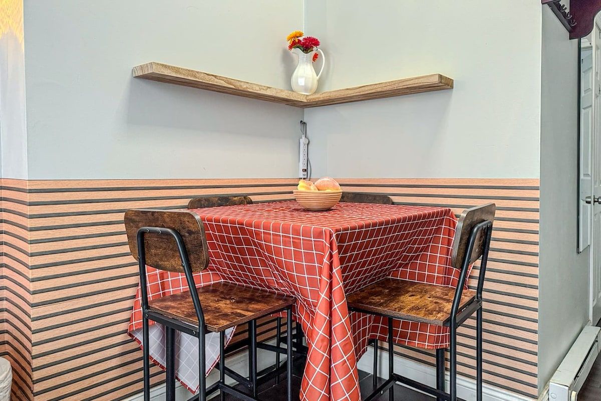 A dining area with a table set for two, chairs, a vase with flowers, and a fruit bowl.