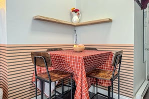 Een eethoek met een tafel voor twee, stoelen, een vaas met bloemen en een schaal met fruit.