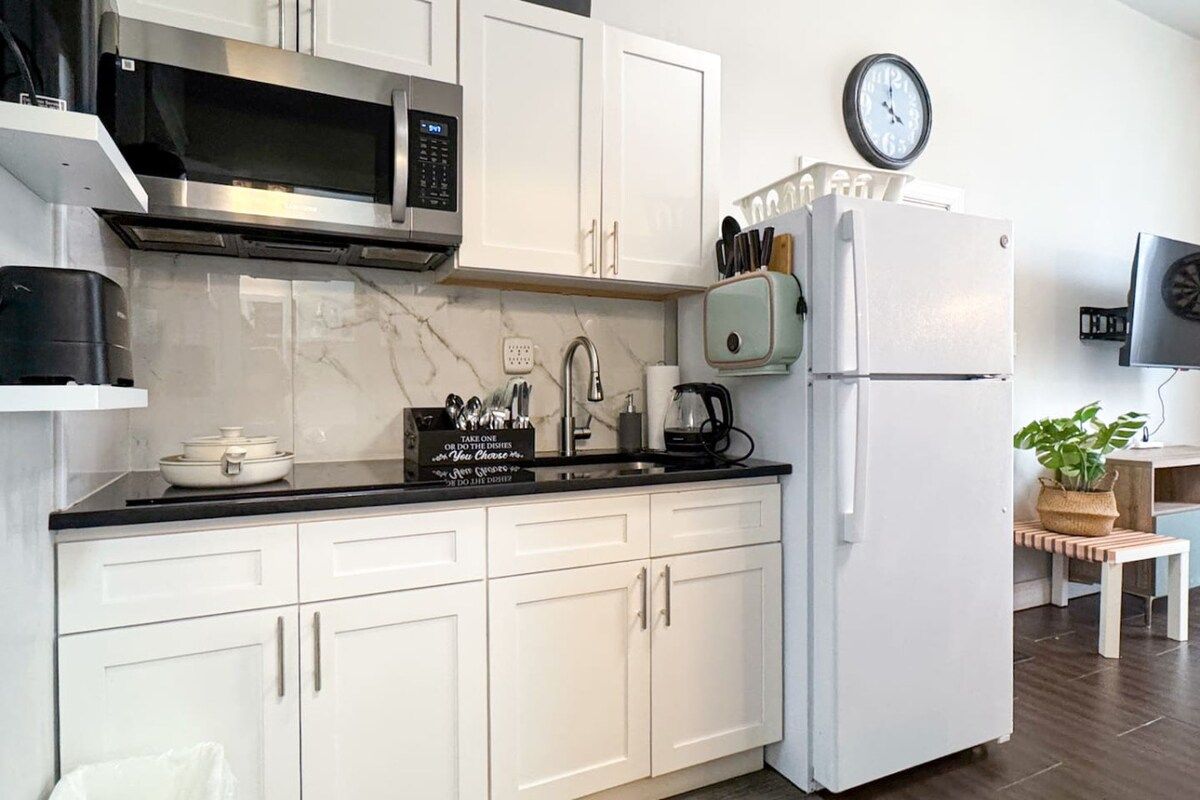 A modern kitchen with white cabinets, a stainless steel microwave, a white refrigerator, and a clock on the wall.