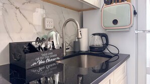 Une cuisine avec un dosseret en marbre, un plan de travail noir, un évier, une machine à café et un bloc à couteaux agrémenté d’une citation inspirante.