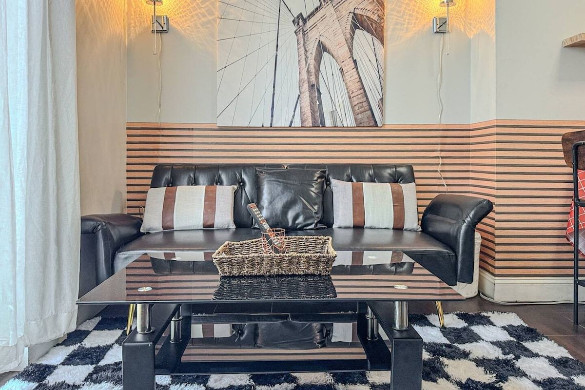 A modern living room with a black leather sofa, a glass coffee table, and a large abstract painting on the wall.