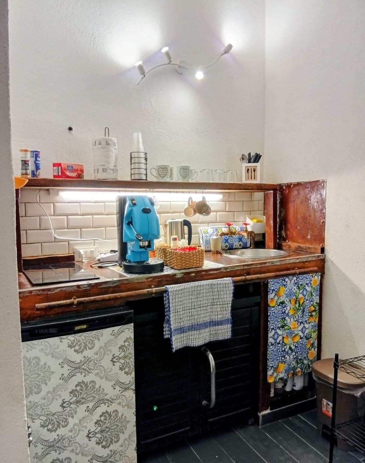 A compact kitchen with a built-in dishwasher, a coffee maker, and a kettle on the counter.