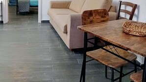 Un salon avec un canapé beige, une table à manger en bois avec des chaises, une horloge au mur et des affiches motivantes.