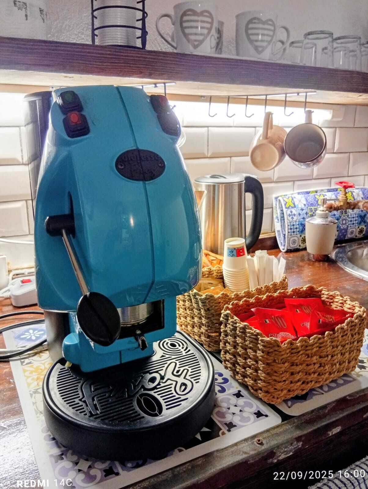 A kitchen with a blue coffee machine, a basket of red items, and a coffee pot on the counter.